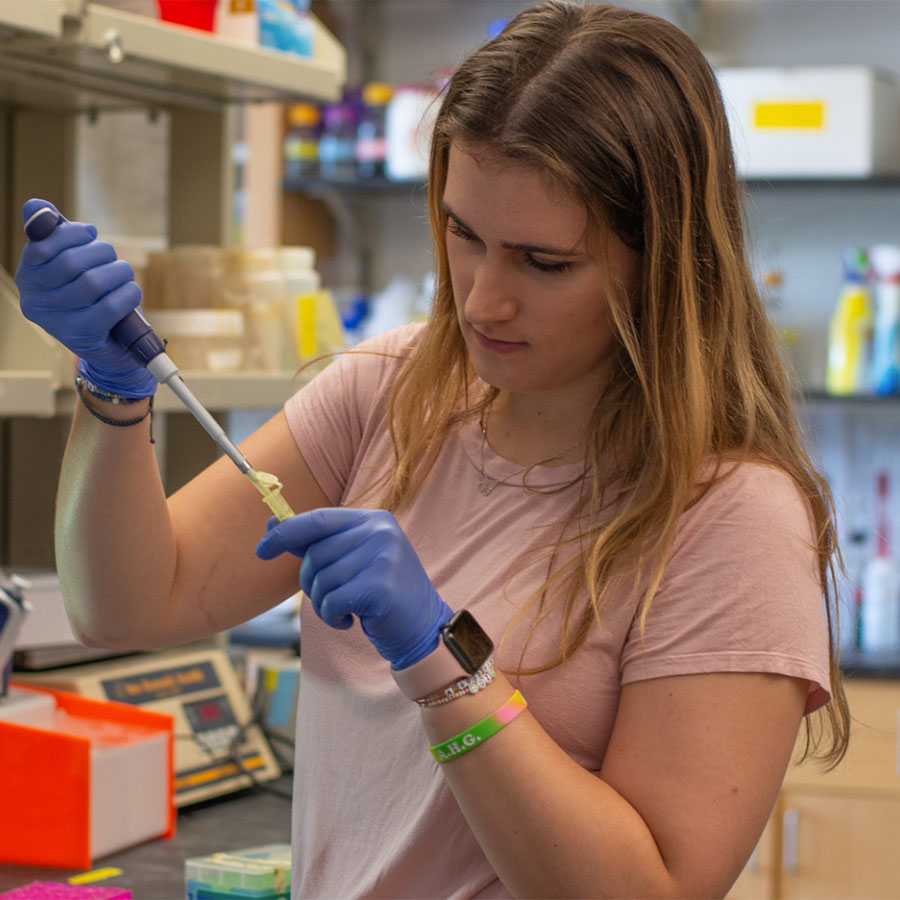 A young adult works with a pipette in a lab setting.