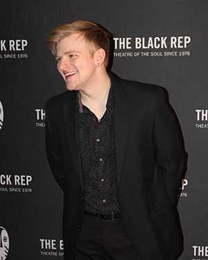 An actor wearing all black walks the red carpet with a backdrop that says THE BLACK REP THEATRE OF THE SOUL SINCE 1976 behind him