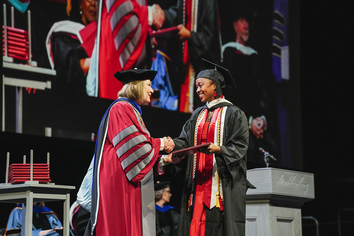 A college president shakes hands with a college graduate receiving a diploma
