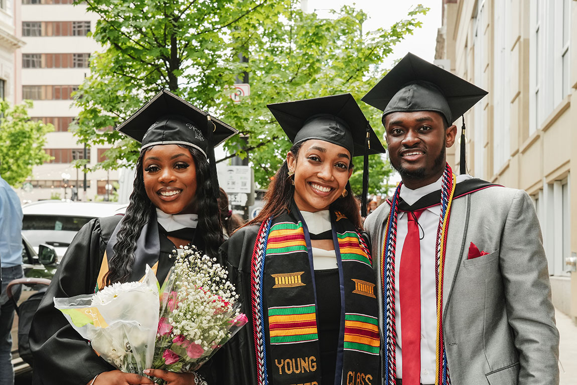Three college graduates smile for a photo after Commencement